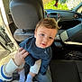 baby, child, car_interior, blue_sweater, person, lap, hand, curly_hair, seat, sunlight, open_car_door, casual_clothing, indoor, portrait, cute, young_child, socks, human, looking_at_camera, seated