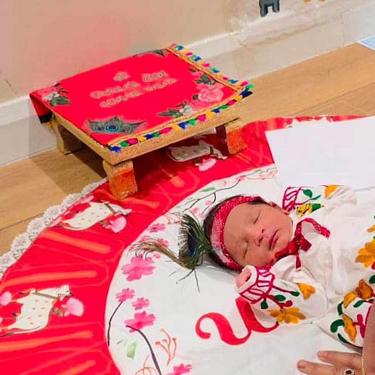 Krish joined the competition — help win amazing prizes! animal_pattern, baby, child, colorful_clothing, decorative_stool, floor, flower_pattern, hand, headband, indoors, mat, newborn, peaceful, poster, rings, sleeping, text, traditional_attire, wall, wooden_floor