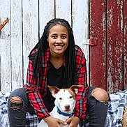 Callie joined the competition — help win amazing prizes! person, dog, smiling, braids, plaid_shirt, ripped_jeans, boots, white_dog, blue_collar, sitting, blanket, wooden_wall, rustic, outdoor, pet, leash, casual_clothing, happy, portrait, companion