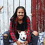person, dog, smiling, braids, plaid_shirt, ripped_jeans, boots, white_dog, blue_collar, sitting, blanket, wooden_wall, rustic, outdoor, pet, leash, casual_clothing, happy, portrait, companion