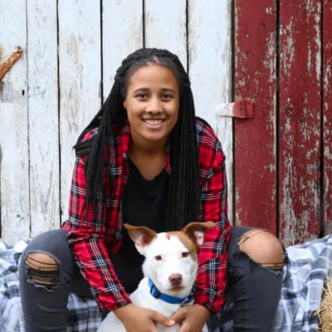 Callie joined the competition — help win amazing prizes! blanket, blue_collar, boots, braids, casual_clothing, companion, dog, happy, leash, outdoor, person, pet, plaid_shirt, portrait, ripped_jeans, rustic, sitting, smiling, white_dog, wooden_wall