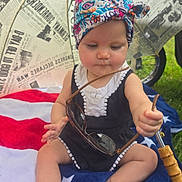Quinn joined the competition — help win amazing prizes! baby, blanket, child, concentration, cute, foot, grass, hand, headwrap, newspaper_print, outdoor, patriotic, person, sitting, stars, stripes, summer, sunglasses, toy, umbrella