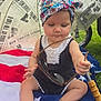 baby, blanket, child, concentration, cute, foot, grass, hand, headwrap, newspaper_print, outdoor, patriotic, person, sitting, stars, stripes, summer, sunglasses, toy, umbrella