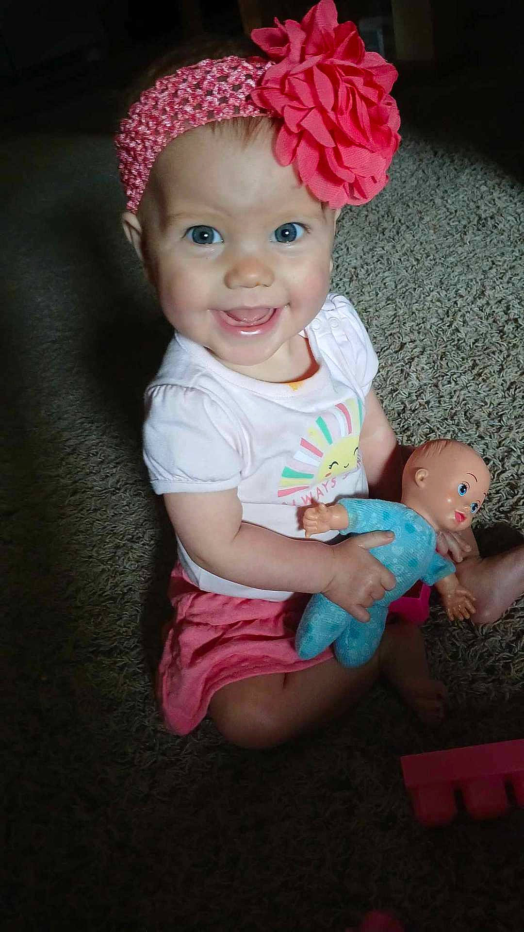 Quinn is registered to the contest to win money with this photo: baby, blue_eyes, carpet, child, cute, doll, flower, happy, headband, indoor, infant, person, pink_skirt, playtime, portrait, sitting, smiling, toddler, toy, white_shirt