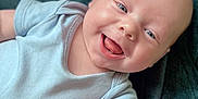 Toby is registered to the contest to win money with this photo: baby, infant, smiling, happy, tongue_out, blue_onesie, blanket, soft_texture, lying_down, cute, child, skin, face, head, arm, closeup, portrait, baby_boy, expression, comfort
