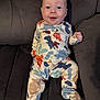 Toby is registered to the contest to win money with this photo: baby, infant, smile, onesie, dinosaur_pattern, couch, furniture, happy, child, indoor, portrait, clothing, sitting, face, cute, person, young, comfort, relax, soft