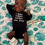 Taisley is registered to the contest to win money with this photo: baby, infant, black_onesie, white_bow, white_socks, blanket, patterned_blanket, face, headband, lying_down, baby_clothing, curious_expression, cute, child, indoors, pacifier_clip, soft_texture, dark_skin, photography, portrait