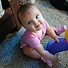 baby, child, infant, sitting, carpet, indoor, portrait, face, blue_eyes, blond_hair, pink_shirt, pink_shoes, purple_toy, toy, laundry_basket, furniture, home, candid, pouting, smiling