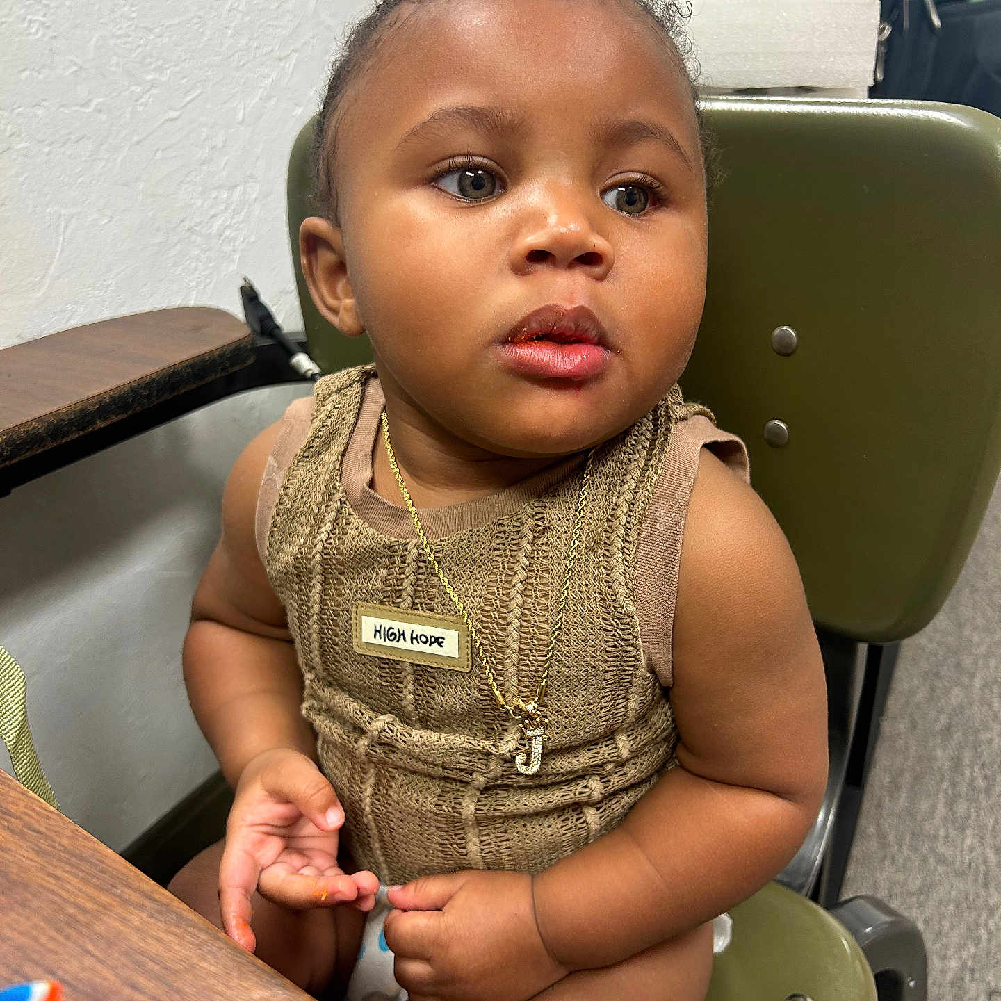 Jhamir is registered to the contest to win money with this photo: badge, brown_clothing, chair, child, curly_hair, cute, expression, face, fingers, green_chair, indoor, jewelry, looking_away, necklace, person, seated, skin, table, toddler, young_child