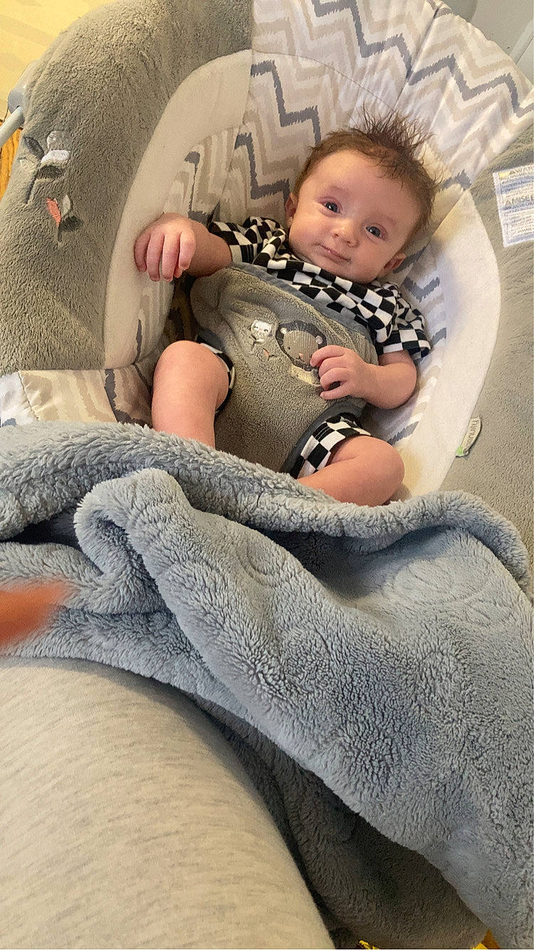 Xavier joined the competition — help win amazing prizes! baby, baby_seat, baby_toys, blanket, checkered, child, clothing, comfort, cozy, cute, hair, indoor, infant, person, portrait, relaxing, seat, smile, soft, young