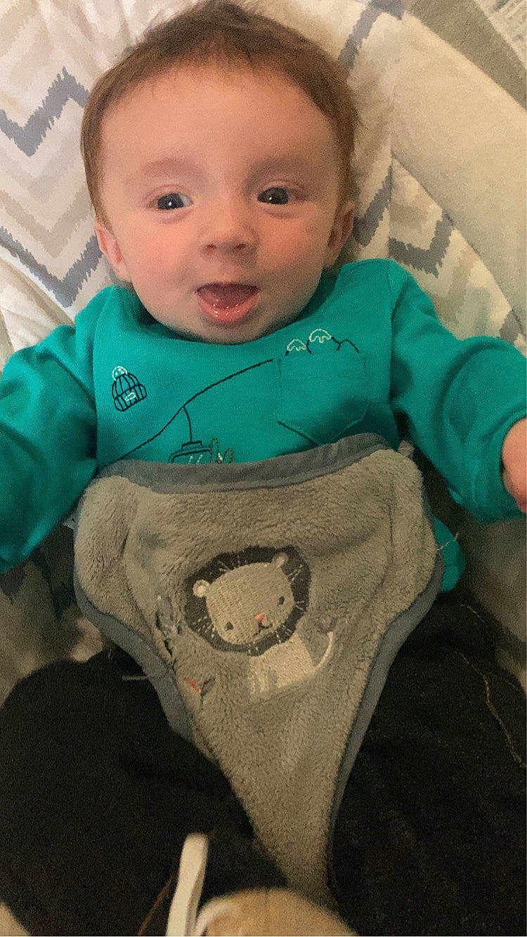 Xavier joined the competition — help win amazing prizes! baby, bib, blanket, blue_eyes, child, clothing, cute, face, happy, indoors, infant, lion_design, lying_down, patterned_background, playful, portrait, smiling, teal_shirt, tongue_out, young