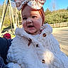 baby, bow_headband, button, cheeks, child, earring, fence, floral_bow, fluffy_coat, happy, infant, outdoors, park, person, playground, portrait, smile, sunlight, trees, wooden_structure
