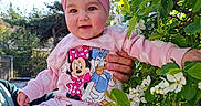 Beatrice a rejoint le concours — aidez-le/la à gagner de superbes lots ! adult_hands, baby, child, cute, donald_duck, face, flowers, garden, green_leaves, hand, headband, holding, minnie_mouse, outdoor, pajamas, pink_clothing, portrait, smiling, turban, white_blossoms