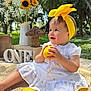 Mis Bas is registered to the contest to win money with this photo: baby, celebration, child, grass, happy, lemon, lemon_pattern, nature, one, outdoor, palm_trees, picnic, sitting, smiling, summer, sunflowers, white_dress, wicker_mushroom, wooden_blocks, yellow_headband
