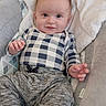 baby, infant, child, smile, face, eyes, hands, clothing, checkered_shirt, pants, socks, blanket, baby_seat, cushion, soft_texture, indoor, portrait, cute, relaxing, happy