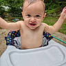 baby, child, wet_hair, high_chair, outdoor, greenery, smiling, happy, polka_dot, seat, arms_up, garden, hose, nature, infant, portrait, cute, playful, summer, water
