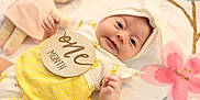 Era Viella is registered to the contest to win money with this photo: apparel, baby, bow, child, cute, doll, eyes, face, floral_blanket, hand, headband, indoors, infant, lying_down, newborn, one_month_sign, portrait, smiling, soft_toy, yellow_clothing