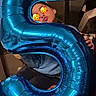 balloon, blue, casual, celebration, child, clothing, cute, face, fun, hand, home, indoor, kid, number_five, party, playful, pucker, sitting, smile, young
