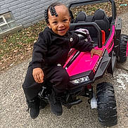 Kennedi is registered to the contest to win money with this photo: toddler, child, smiling, toy_car, pink, black_clothing, nike, outdoor, pavement, brick_wall, beaded_hair, boots, happy, person, play, vehicle, small_car, leaves, casual, daylight