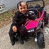 toddler, child, smiling, toy_car, pink, black_clothing, nike, outdoor, pavement, brick_wall, beaded_hair, boots, happy, person, play, vehicle, small_car, leaves, casual, daylight