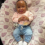 Melanie is registered to the contest to win money with this photo: baby, smiling, infant, clothing, jeans, pink_shirt, socks, blanket, heart_pattern, cute, happy, indoors, child, face, person, seated, pacifier, cozy, soft, comfort