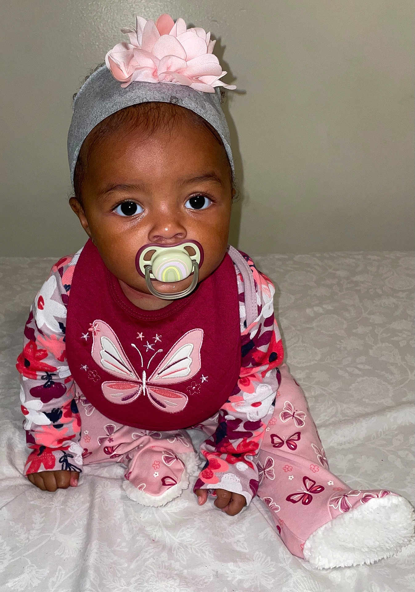 Laylani is registered to the contest to win money with this photo: baby, bib, blanket, butterfly, child, curious, cute, face, flower, foot, hand, headband, indoor, infant, maroon, pacifier, pajamas, patterned_clothing, pink, sitting