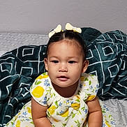 Rebecca is registered to the contest to win money with this photo: toddler, child, girl, dress, hairbrush, hair_bow, bed, blanket, pattern, yellow, white, blue, green, foot, sitting, indoors, curious, person, portrait, cute