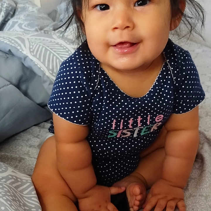 Rebecca joined the competition — help win amazing prizes! baby, child, infant, smiling, sitting, bed, blanket, polka_dot, clothing, phone, indoors, hair, face, hands, feet, onesie, cute, happy, portrait, toddler