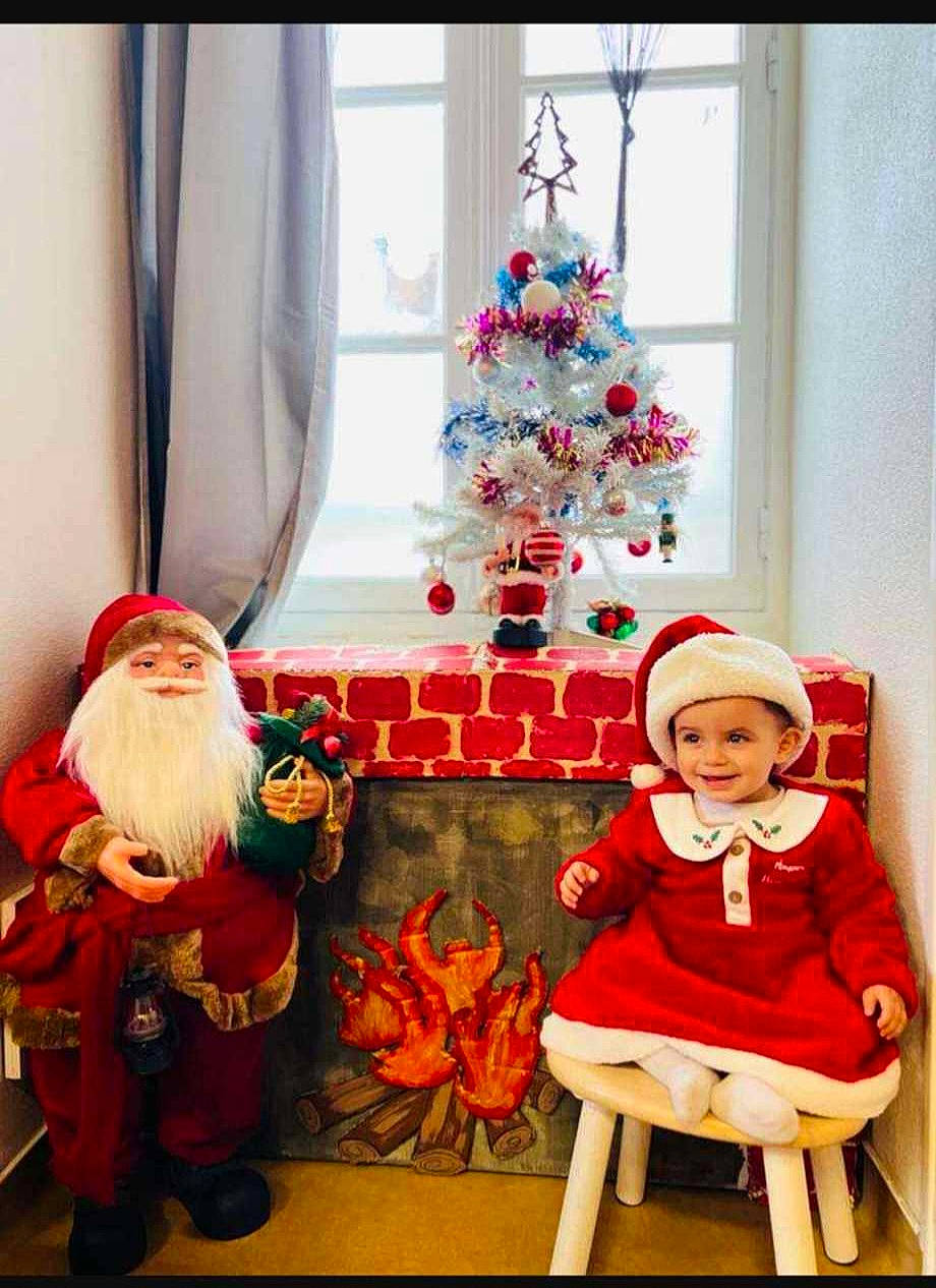 Izia participe au concours pour gagner de l'argent avec cette photo : chair, christmas, christmas_decoration, christmas_ornament, christmas_tree, costume_hat, event, hat, headwear, holiday, holiday_ornament, interior_design, joy, lap, lighting, ornament, person, red, santa_claus, stool