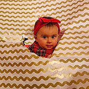 Nina participe au concours pour gagner de l'argent avec cette photo : baby, child, face, headband, red, plaid, pattern, wrapping_paper, hole, curious, peek, indoor, cute, portrait, infant, expression, holiday, festive, smiling, young