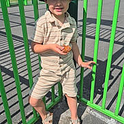 Milo a rejoint le concours — aidez-le/la à gagner de superbes lots ! boy, bucket_hat, casual, child, confident_pose, green_fence, happy, hat, outdoor, pavement, person, playground, sandals, shadow, shorts, smile, snack, striped_clothing, summer_clothing, sunny_day