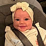 baby, child, smile, headband, bow, car_seat, safety_strap, clothing, cute, infant, portrait, happy, indoors, close_up, face, person, seat, strapped, apparel, newborn