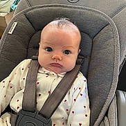 Mia participe au concours pour gagner de l'argent avec cette photo : baby, car_seat, child, infant, face, straps, white_clothing, red_hearts, pout, curious_eyes, indoor, seat, safety_harness, person, cute, expression, head, young_child, fabric, soft