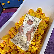 Mary joined the competition — help win amazing prizes! baby, bathtub, rubber_duck, yellow, cushion, white_clothing, headband, purple_rug, pink_rug, blue_wall, toy, child, indoor, playful, cute, infant, soft_texture, patterned_cushion, relaxed, colorful