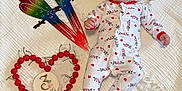 Mary is registered to the contest to win money with this photo: baby, infant, onesie, headband, red_bow, smile, face, parrot_decor, cherries, heart_shape, wooden_plaque, 7_months, white_blanket, texture, milestone, cute, lying_down, happy, celebration, indoors