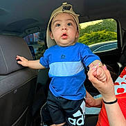 Uriel joined the competition — help win amazing prizes! toddler, child, boy, cap, blue_shirt, shorts, sneakers, car_interior, hand_holding, adult_hand, seat, window, greenery, expression, curious, standing, casual_clothing, daylight, person, portrait