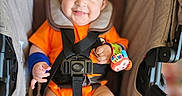 Bodoquito is registered to the contest to win money with this photo: baby, baby_accessory, blue_socks, child, colorful, cushion, cute, happy, head_support, indoors, infant, orange_clothing, person, portrait, safety_harness, seatbelt, seated, smiling, stroller, wrist_rattle