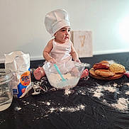 Bodoquito joined the competition — help win amazing prizes! apron, baby, baking, chef_hat, child, cookies, cute, doughnut, flour, food, indoor, kitchen, messy, mixing_bowl, pastries, person, playful, sitting, spoon, table