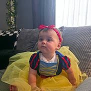 Isabella is registered to the contest to win money with this photo: baby, child, costume, dress, headband, tutu, yellow, red, blue, couch, indoor, curtains, soft_light, sitting, cute, portrait, person, infant, toddler, holiday