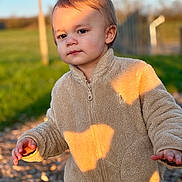 Marceau participe au concours pour gagner de l'argent avec cette photo : child, toddler, outdoor, sunlight, fleece_jacket, beige_clothing, curious, pathway, golden_hour, shadow, nature, portrait, person, young_child, casual_clothing, daylight, expression, walking, grass, background
