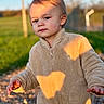 child, toddler, outdoor, sunlight, fleece_jacket, beige_clothing, curious, pathway, golden_hour, shadow, nature, portrait, person, young_child, casual_clothing, daylight, expression, walking, grass, background