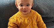 Marceau participe au concours pour gagner de l'argent avec cette photo : toddler, child, sweater, knitted, mustard_yellow, pants, beige, couch, sofa, indoor, portrait, seated, cute, smiling, young_child, face, person, cozy, home, casual