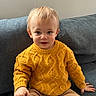 toddler, child, sweater, knitted, mustard_yellow, pants, beige, couch, sofa, indoor, portrait, seated, cute, smiling, young_child, face, person, cozy, home, casual