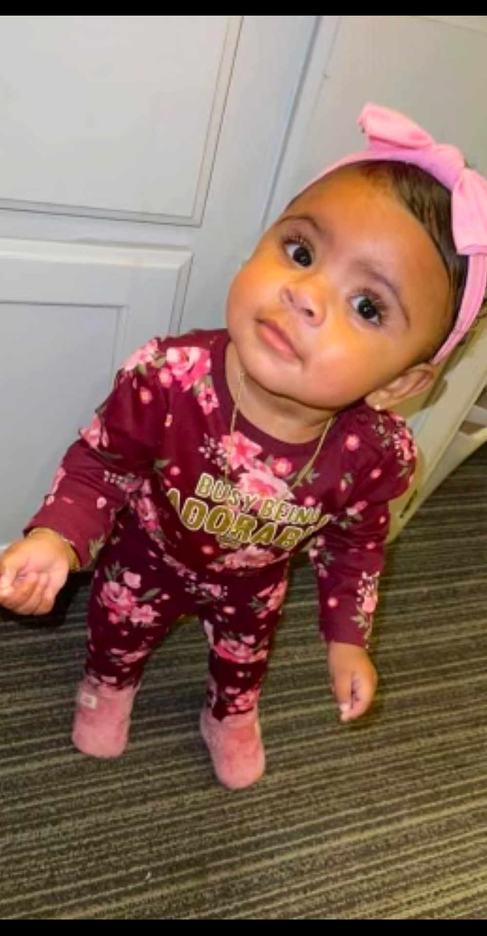 Willa-Jah joined the competition — help win amazing prizes! toddler, child, pink_bow, floral_outfit, slippers, carpet, indoors, curious, standing, big_eyes, maroon, baby, headband, cute, looking_up, young_child, person, floor, portrait, clothing