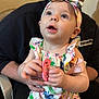 baby, child, infant, headband, pacifier, adult, hands, clothing, sitting, indoor, person, cute, curious, face, light_skin, holding, colorful, patterned, young, portrait