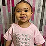 toddler, child, smiling, pink_shirt, purple_skirt, heart_pattern, standing, happy, indoor, portrait, cute, young_child, person, background_pattern, colorful, clothing, face, eyes, joyful, innocent