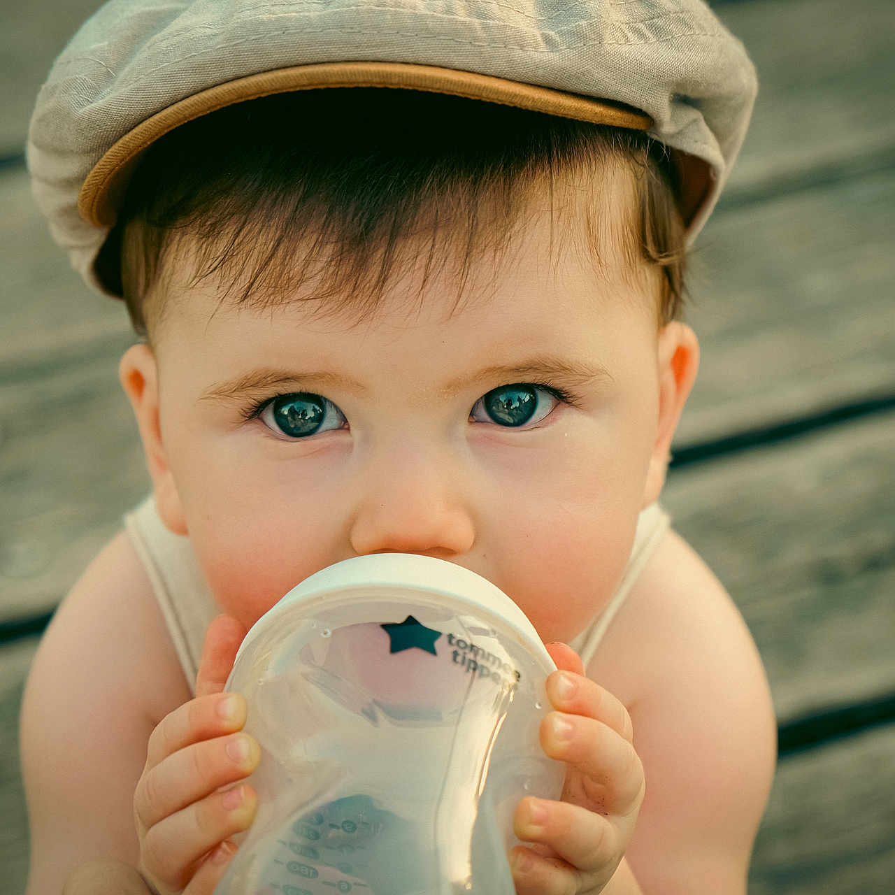 éli participe au concours pour gagner de l'argent avec cette photo : baby, blue_eyes, bottle, cap, casual, child, close_up, cute, drinking, face, hands, headwear, holding, infant, outdoor, person, portrait, skin, wooden_floor, young