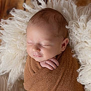 Thibault a rejoint le concours — aidez-le/la à gagner de superbes lots ! newborn, baby, infant, sleeping, wrapped, blanket, brown, white, fluffy, cushion, wooden_floor, peaceful, cute, portrait, closeup, soft_texture, resting, indoors, child, hands