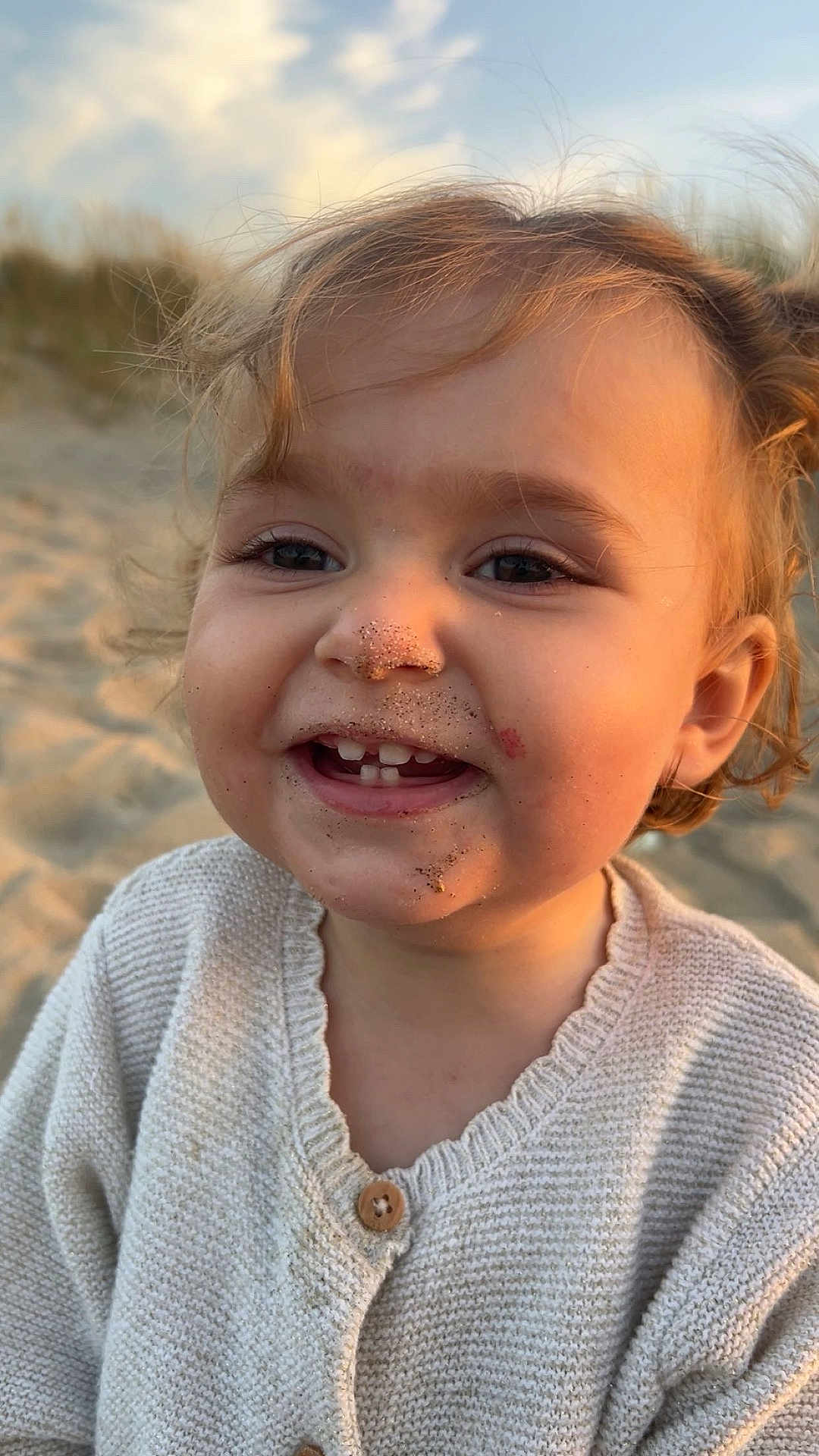 Mia participe au concours pour gagner de l'argent avec cette photo : toddler, child, face, smile, sandy_face, knitted_sweater, beach, outdoor, sunset, golden_hour, happy, cute, portrait, childhood, nature, warm_light, curly_hair, close_up, skin, young