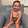 toddler, child, smiling, happy, sitting, armchair, clothing, suspenders, shorts, face, person, indoor, furniture, baby, cute, rosy_cheeks, hair, window, home, portrait